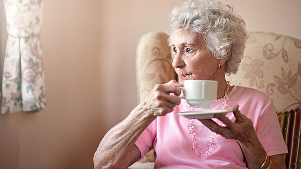 An elderly lady smiling whilst holding a cup of tea.
