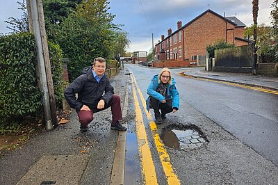 Cllrs Will Frass and Jane Brophy crouching next to a pothole on Deansgate Lanes Cllrs Will Frass and Jane Brophy crouching next to a pothole on Deansgate Lanes